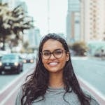 A young woman with glasses smiling on a city street, embracing urban lifestyle.